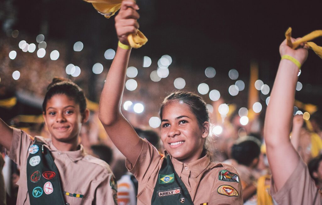 Jovens desbravadoras uniformizadas, com sorrisos e braços erguidos, durante o VI Campori Sul-Americano da Divisão Sul-Americana de Desbravadores.